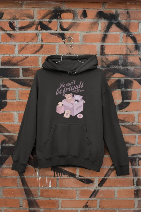 Cute black hoodie with a pink teddy bear graphic and the text "We can't be friends wait for your love" on a graffiti brick wall background.